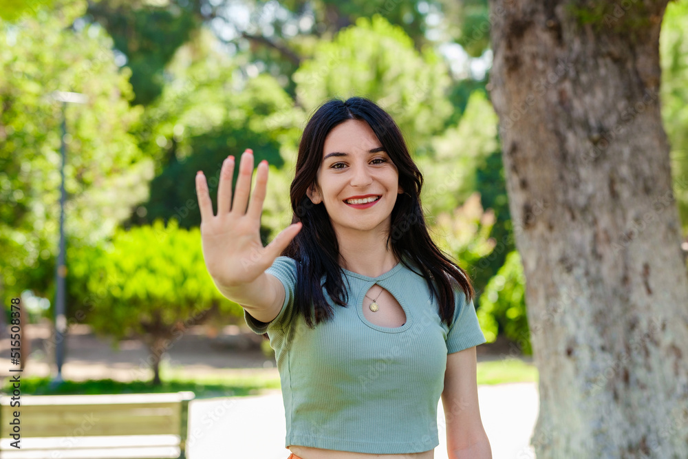 Young brunette girl smiling happy wearing turquoise t-shirt standing on city park, outdoors showing and pointing up with fingers number five while smiling confident and happy. Young brunette girl smiling happy wearing turquoise t-shirt standing on city park, outdoors showing and pointing up with fingers number five while smiling confident and happy.