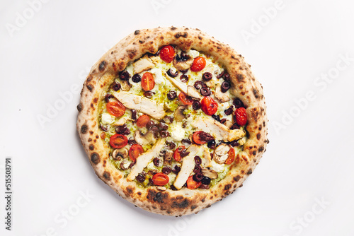 Top view of pizza topped with tomato, chicken, olives and mushrooms on a white background