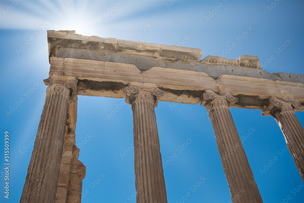 An ancient greek stone-made arch from a temple with the bright sunlight above creating sun rays over the whole picture. 