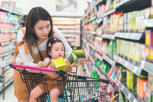 Asian mother and her daughter buying food at huge supermarket , Baby sit in trolley, Family shopping concept.