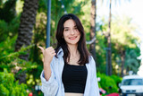 Happy woman wearing striped shirt standing on city park, outdoors smiling with happy face looking at the camera and pointing to the side with thumb.