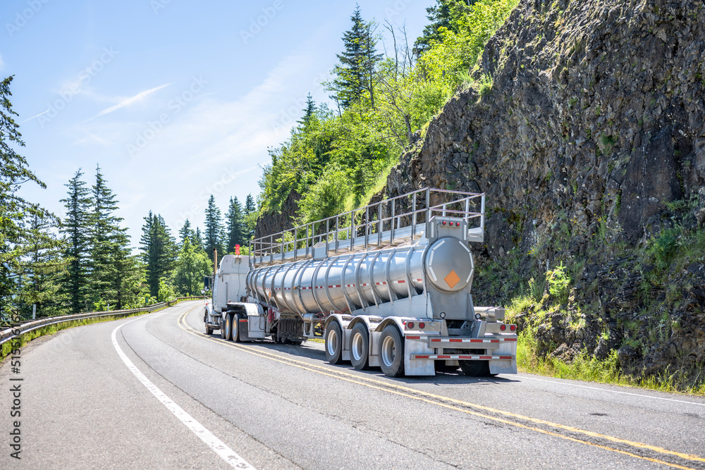 Industrial grade big rig semi truck tractor transporting cargo in cone fertilizer bulk semi trailer with stiffeners and safety ladder from above turning on the winding mountain road