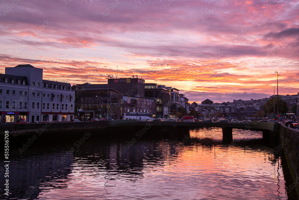 Cork City, Ireland - Oct 12th, 2021: Beautiful view of River Lee reflections, colors and lights at sunset time. Purple sky. Traffic at the bridge