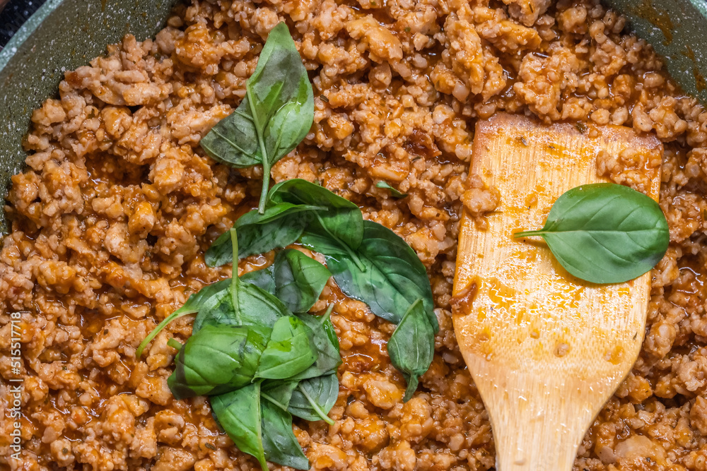 Basil leaves in a green frying pan with minced meat tomato sauce and a wooden spatula. Basil leaves in a green frying pan with minced meat tomato sauce and a wooden spatula.