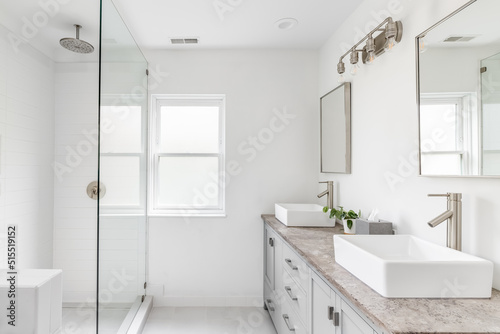 An elegant  renovated bathroom with white sinks  grey vanity  granite countertop  and bronze hardware  faucets and light. 