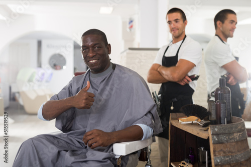 Portrait of happy African-American male client of barbershop after haircut performed by skilled hairstylist