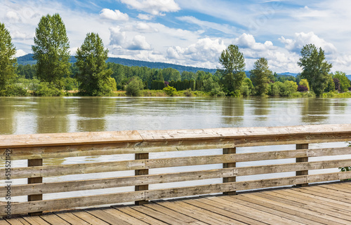 Perspective view of a wooden pier on the river in a summer park.