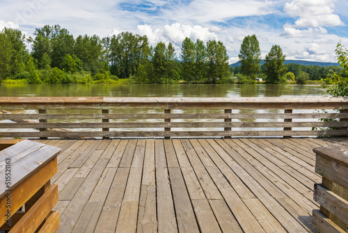 Perspective view of a wooden pier on the river in a summer park.