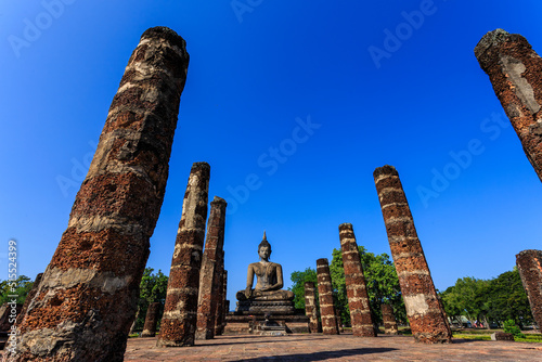 Beautiful scenic view of Wat Mahathat in Sukhothai historical park, Sukhothai, Thailand with sitting Buddha between ruins. UNESCO and World Heritage site. Travel concept.