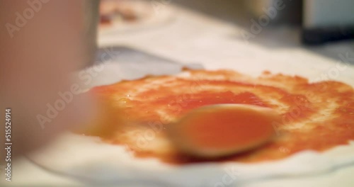 Close-up of adding pizza sauce to pizza base - preparing food in kitchen