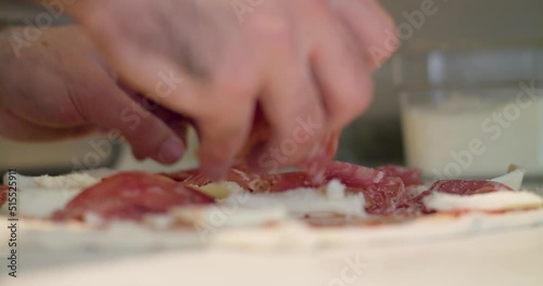Close-up of adding pizza toppings to a pizza base with pepperoni and cheese