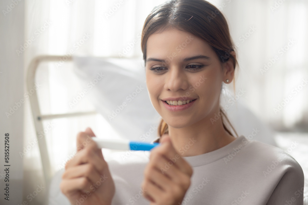 Happiness young asian woman taking pregnancy test while excited and satisfied in the bedroom at home, happy mother with smile and expression with love, ovulation and maternity, medical concept.