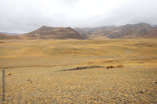 Hilly dried steppe and mountain range with peaks in thunderclouds.