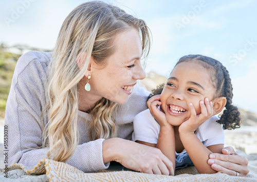Mature foster mother and her adopted daughter smiling and lying on the beach together. Woman and her cute little girl bonding during a summer day out in the sun. Face to face single parent and child