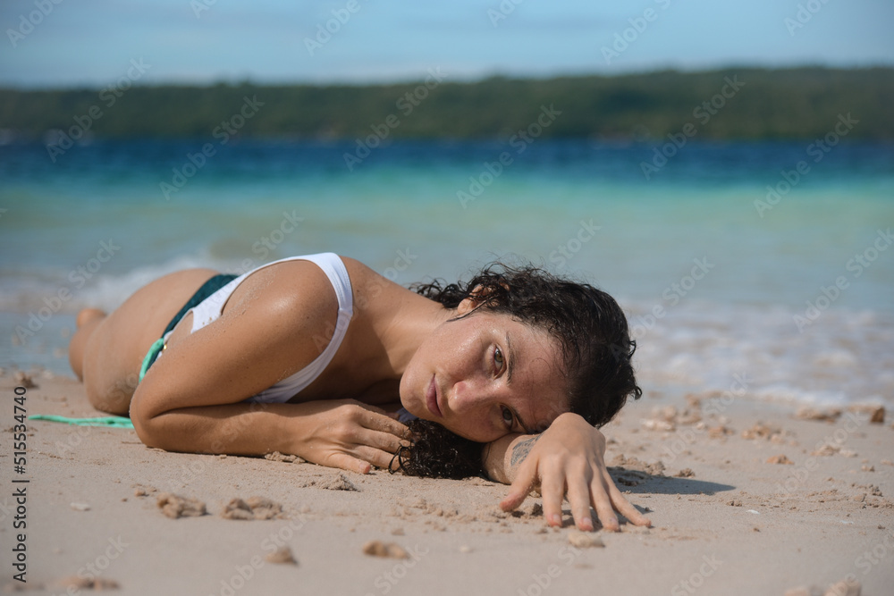 Fototapeta premium Sexy female in a white bikini on a tropical beach. A curly woman enjoys during her summer holiday in the Philippines. Brunette girl in swimsuit relaxing at the water.