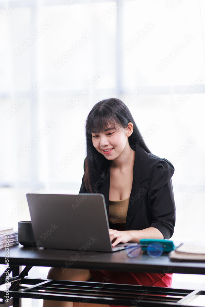 Portrait of a smiling Asian Business woman using modern technology, working over the laptop.