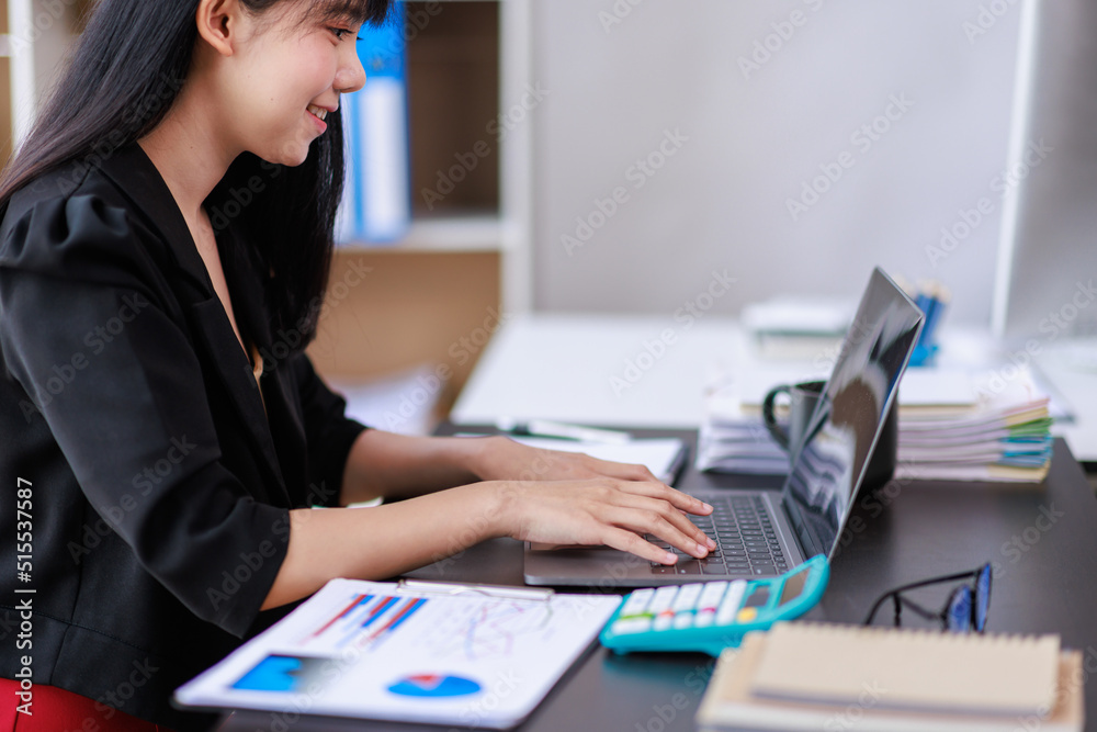Portrait of a smiling Asian Business woman using modern technology, working over the laptop.