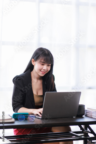 Portrait of a smiling Asian Business woman using modern technology, working over the laptop.