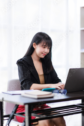 Portrait of a smiling Asian Business woman using modern technology, working over the laptop. © David