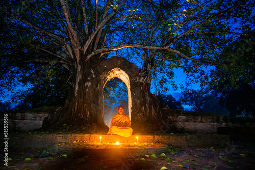 A Thai monk made meditating at an abandoned temple, the old entrance has a banyan tree. Landmark of the ancient city of Ayutthaya, Thailand.