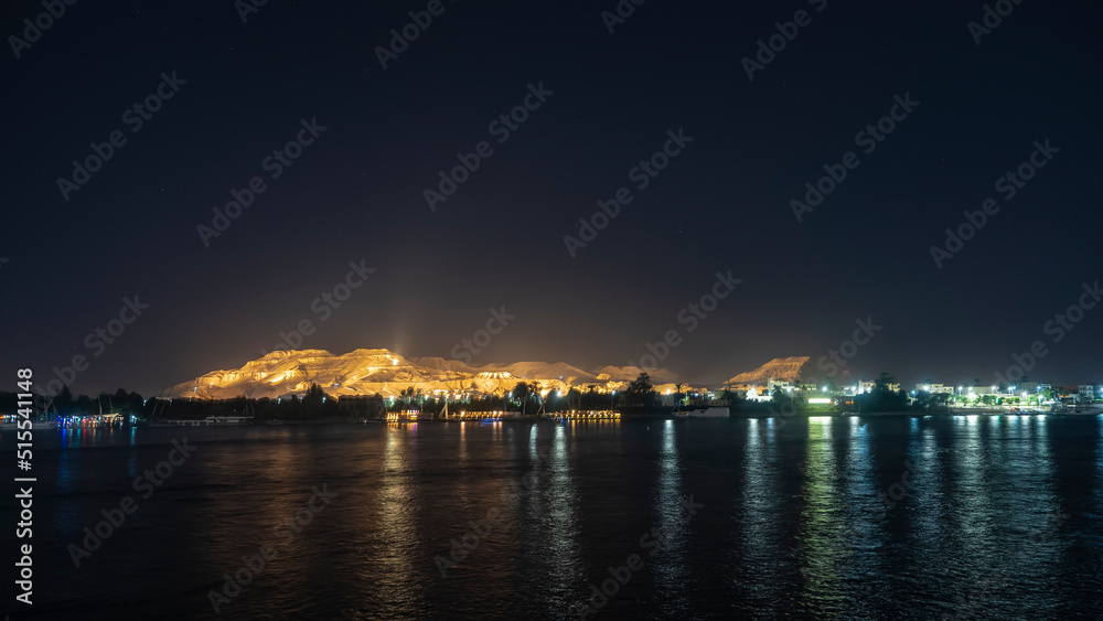 A night in Egypt. The sand dune is highlighted against the dark sky. The ships are moored off the coast of the Nile. Glare and reflection on the water. Copy space.  Aswan