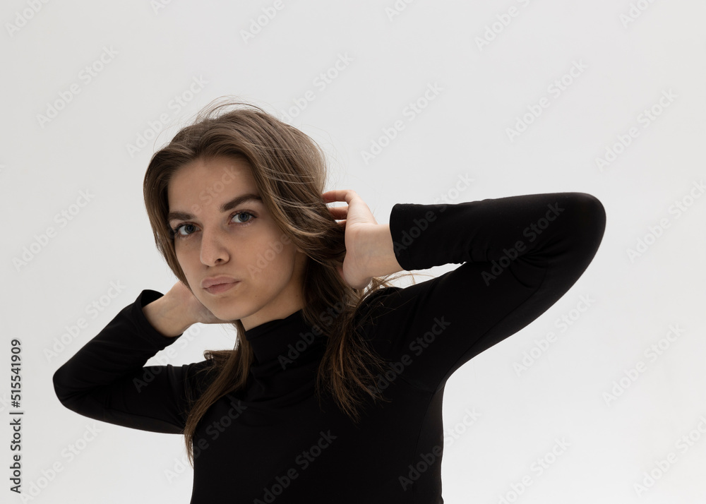 portrait of a beautiful tanned brunette looking into the camera straightening her hair with her hands standing on a white background portrait of a beautiful tanned brunette looking into the camera straightening her hair with her hands standing on a white background