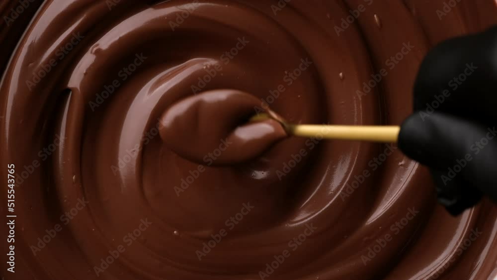Hand stirring melted dark chocolate with golden spoon, close up. Liquid hot chocolate. Confectioner prepares chocolate dessert, glaze
