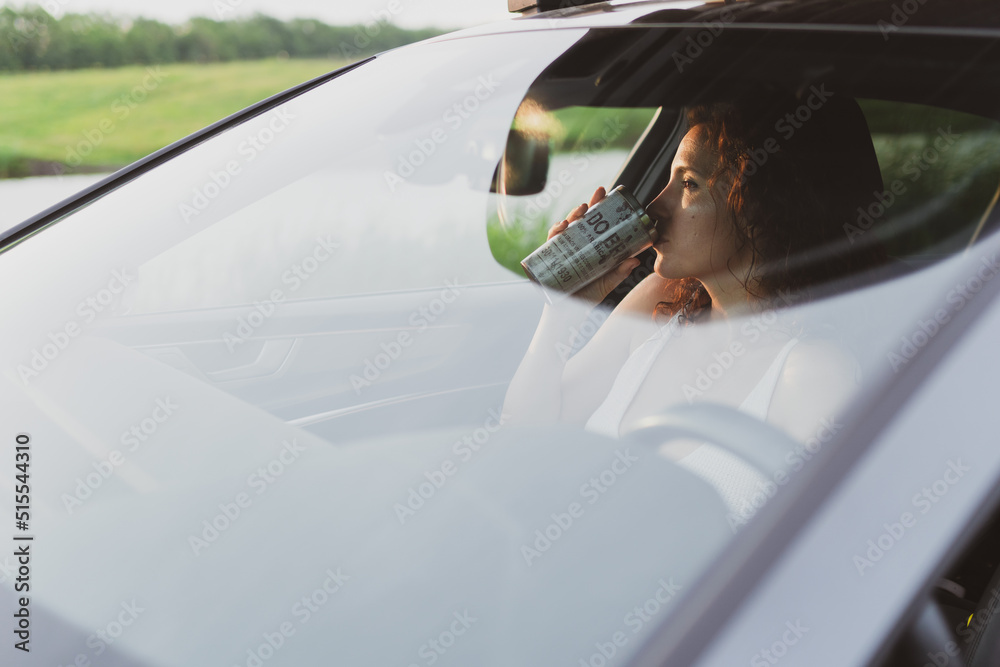 Naklejka premium beautiful young woman travel on the roads by car, stopped at the side of the road and look at the map, drink coffee from a thermos. Vacation concept