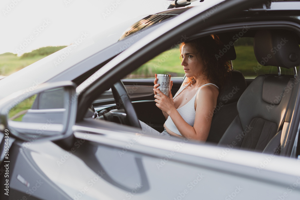 Naklejka premium beautiful young woman travel on the roads by car, stopped at the side of the road and look at the map, drink coffee from a thermos. Vacation concept