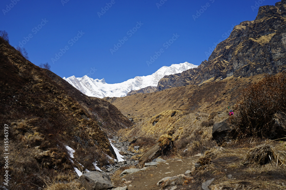 Rocky trail pathway with natural landscape view of snowcapped mountain range with cloudy blue sky- Himalayas ridge, Nepal