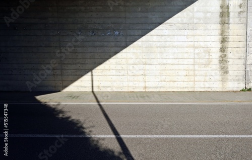 Grunge concrete wall of an underpass divided in two by the shadow of the bridge. Cement sidewalk and two lane road in front. Background for copy space photo