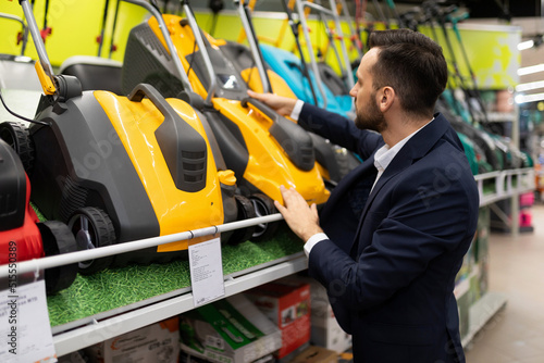 a customer in a gardening tool store examines the features of lawn mowers