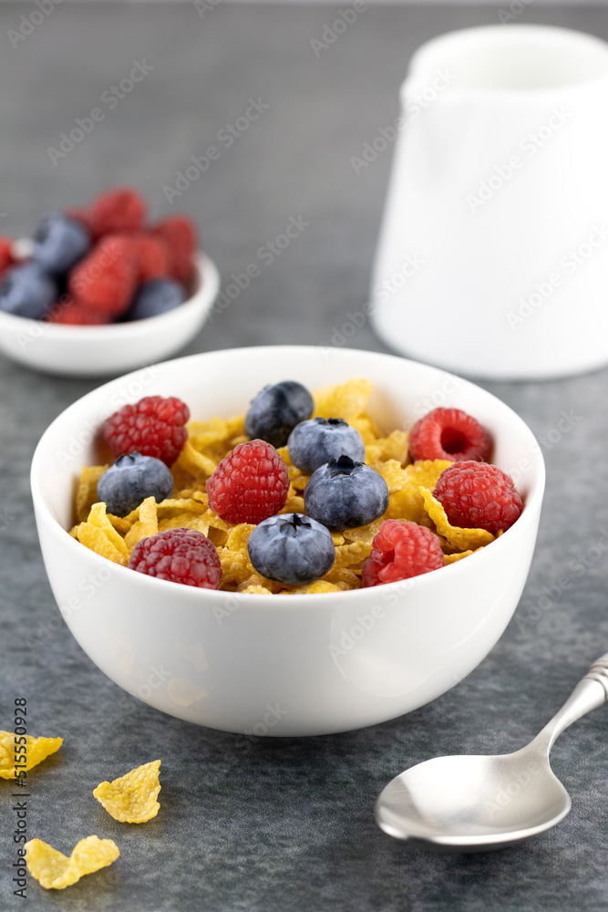 Corn flakes and fresh berries: blueberries, raspberries, milk on a gray background, side view. Healthy breakfast concept. Corn flakes and fresh berries: blueberries, raspberries, milk on a gray background, side view. Healthy breakfast concept.