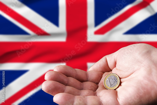 Coin one euro in the hand of a man, the flag of Britain on the background