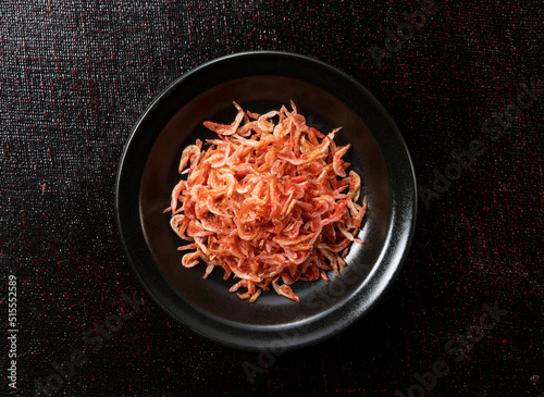 Dried sakura shrimps on a plate placed on a black background.