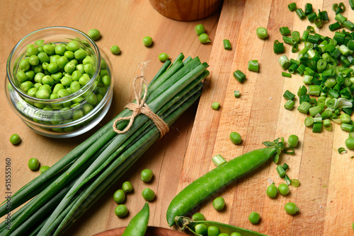 vegetables on a wooden kitchen board, sliced green onions, peas on a wood background, concept of fresh and healthy food, still life