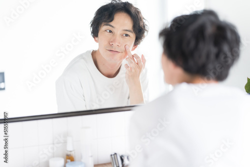 アジア人男性メンズビューティー、頬に手をあてて鏡を見ている photo