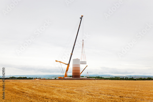 Building and assembling a construction wind turbine by crane. Farmland with construction work at the windfarm in W  rrstadt  Germany. Energy saving concept from wind turbine construction with cloud sky