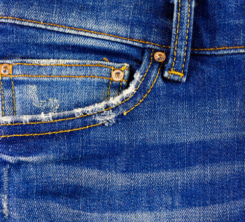 Jeans with frayed pockets and yellow stitching close-up.