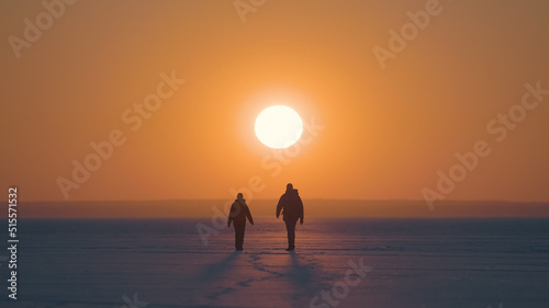 The man and woman going on the snow field on sunset background