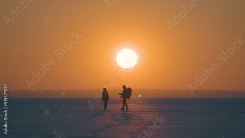The two travelers walking through the snow field on sunset background
