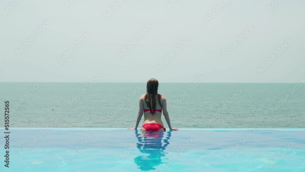 Vacation Girl Relaxes on Edge of Infinity Pool Enjoying Amazing Sea View. Concept Of Comfortable Luxury Rest. Vacation Girl Relaxes on Edge of Infinity Pool Enjoying Amazing Sea View. Concept Of Comfortable Luxury Rest.