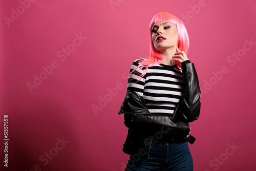 Sensual punk adult wearing rocker leather jacket in studio, expressing carefree funky fashion style. Attractive beautiful lady with trendy clothes and stylish pink hair, cute makeup. photo