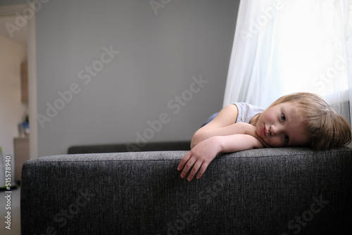 Sad kid is bored on couch in living room.