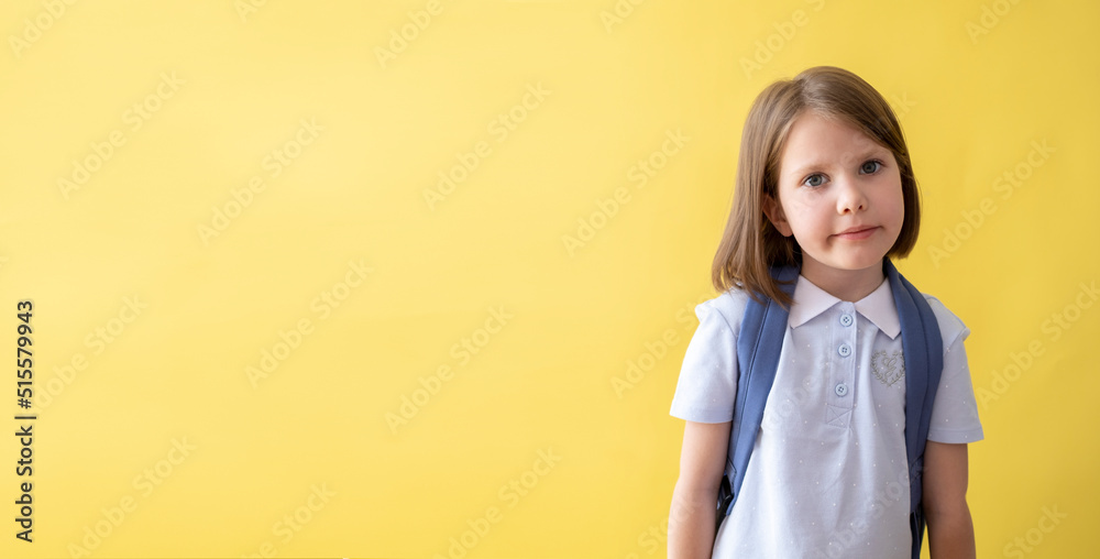 Beautiful girl with a backpack on a yellow background. Soon to school. The concept of school education.
