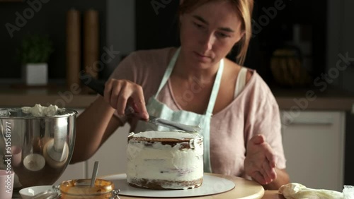 Beautiful young caucasian woman decorating cake with professional tools. Confectioner in the modern stylish kitchen photo