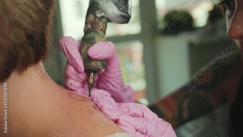 A tattoer makes a tattoo to a client's back. Close up of hands in latex gloves and tattoo machine. Real time. photo