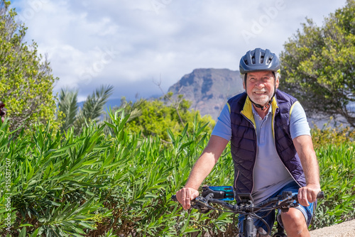 Happy active senior man with electric bicycle running outdoors in the park wearing helmet and sunglasses enjoying healthy lifestyle. #515587507