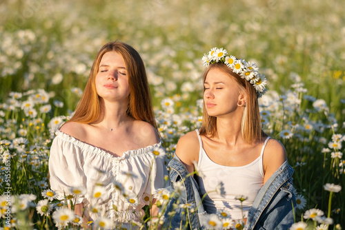 Two girls enjoying a summer day in a field of daisies. Girlfriends hugging and laughing in nature. A same-sex couple happily walking outdoors.