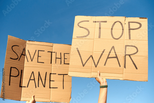 Two Cardboard Signs saying Save the planet, and Stop War. Held by hands on sky background